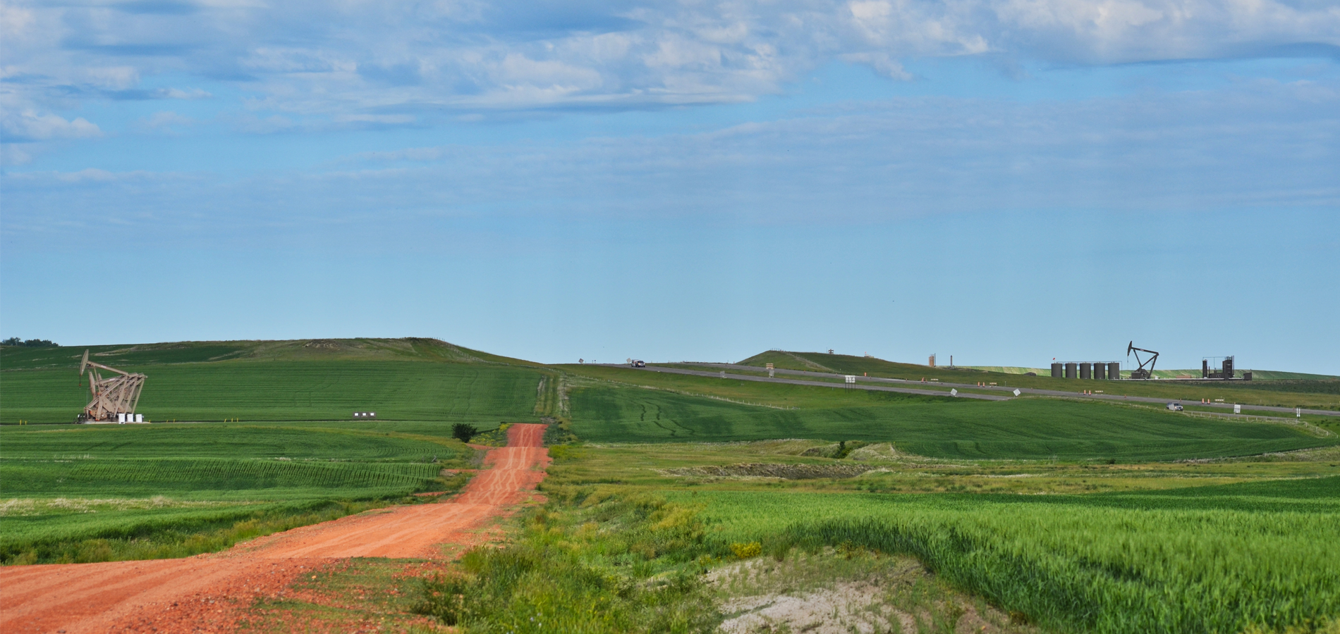 A gravel road cuts through fields with oil wells in North Dakota